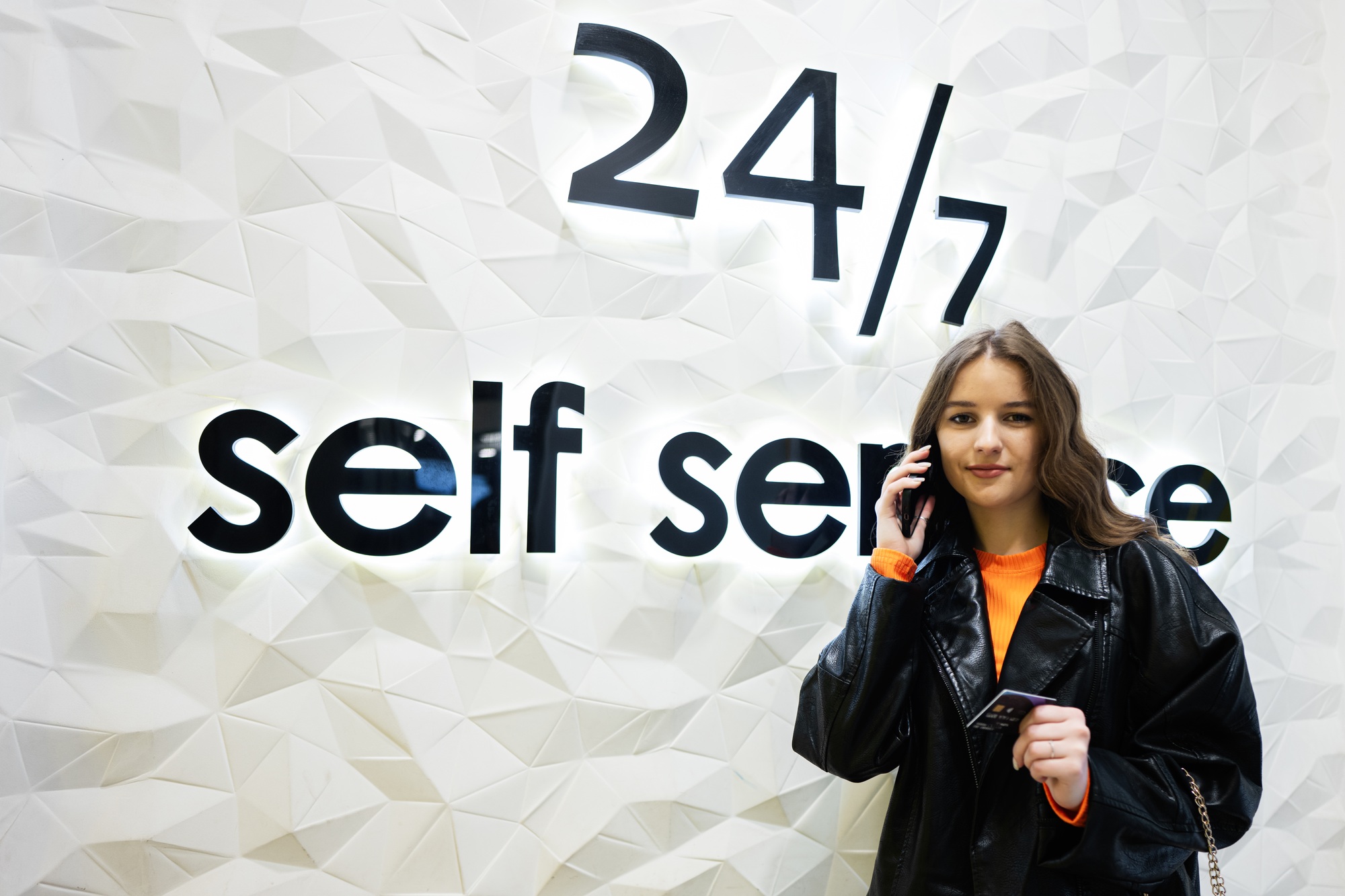 Young brunette girl with credit card against 24 7 self service bank. Round the clock support.